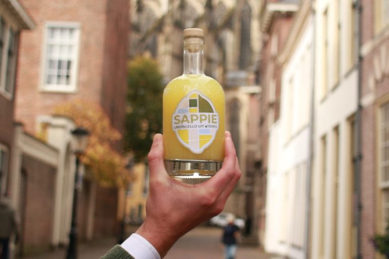 Sappie bij de domkerk Heldere fles met gele drank, gepositioneerd op een straat bij de Domkerk