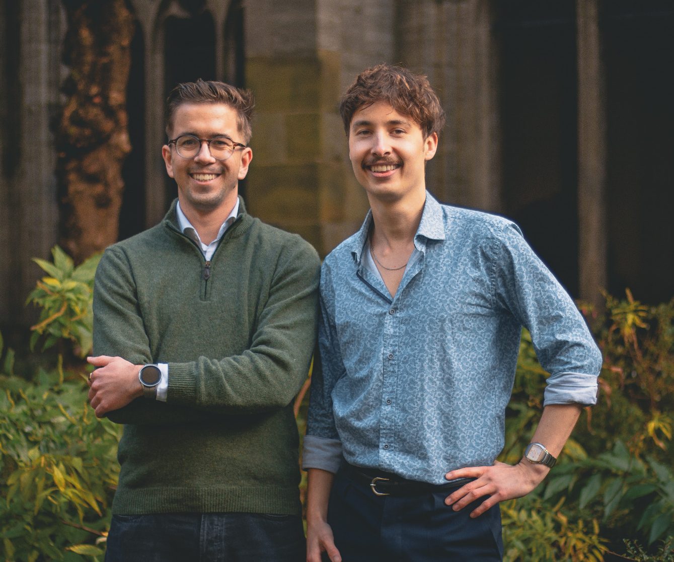 Oscar & Jesse - Eigenaren van Sappie limoncello Twee mannen met glimlachen, staand in een groene omgeving met planten op de achtergrond.